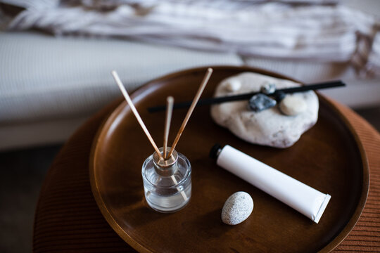 Home liquid glass bottle diffuser with sticks on wooden tray and hand lotion in living room. Spa aromatherapy.