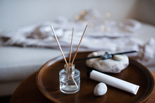 Home liquid glass bottle diffuser with sticks on wooden tray and hand lotion in living room. Spa aromatherapy.