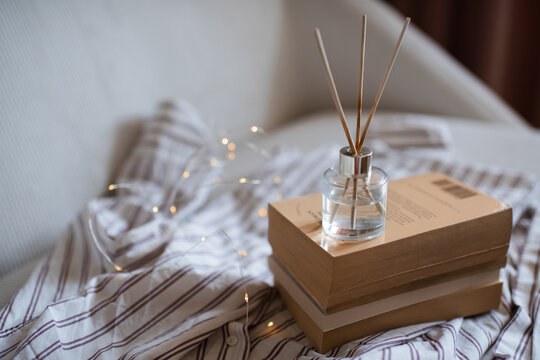 Aroma liquid glass bottle diffuser with wooden sticks on stack of old paper books in living room. Aromatherapy.