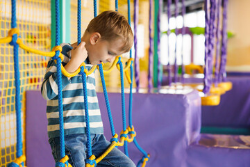 Naklejka premium Young boy climbing rope structure at indoor playground