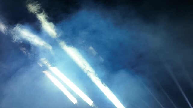 Bright Light Beams Piercing Through Smoke in the Night Sky. Professional Stage Lighting with Beams and Fog Effect at Night