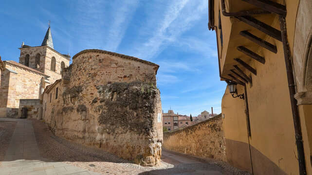 A street in Zamora leading toward the Church of San Cipriano, with its Romanesque apse and bell tower rising above historic stone walls under a clear blue sky, Zamora, Spain