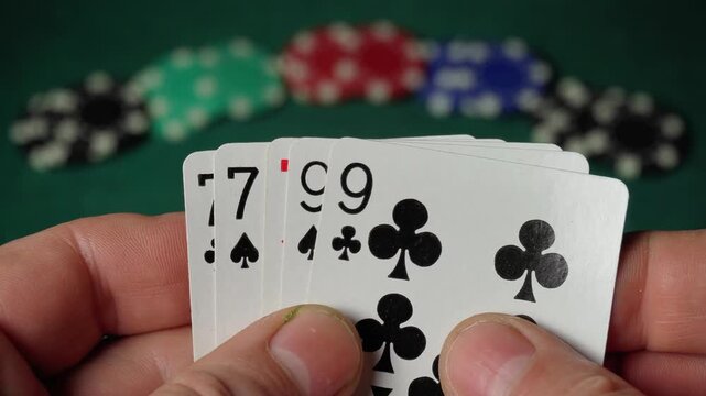 Close-up of hands holding playing cards showing a sequence of numbers, with poker chips in various colors blurred in the background