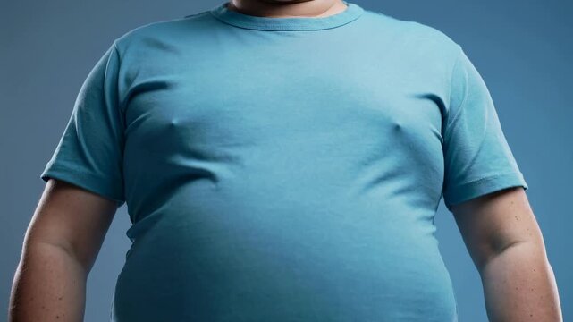 Close-up of an overweight man's torso wearing a tight blue t-shirt against a solid blue background, highlighting his large belly and body shape.
