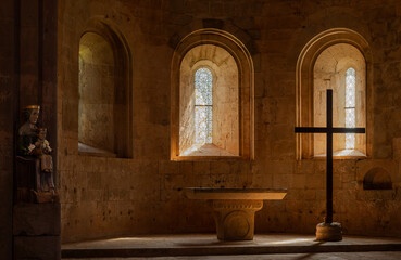 Obraz premium Le Thoronet, Var, France : Romanesque chapel interior with stone altar, cross silhouette and stained glass windows in warm spiritual light
