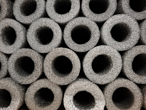 Stacked grey foam insulation pipes showing circular cross sections and a porous material texture in a storage space
