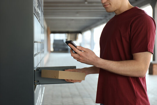 Courier putting cardboard box into parcel locker outdoors, closeup