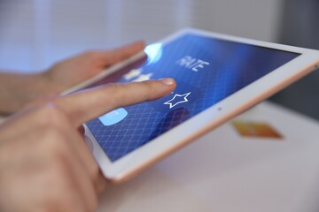 Woman giving four-star rating on tablet at white table indoors, closeup