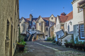 Naklejka premium Narrow cobblestone lane flanked by historic stone cottages and colourful traditional buildings in a Scottish coastal village.