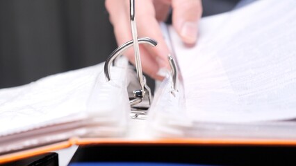 Hand opening a ring binder, organizing and managing important documents, showcasing a close up view...