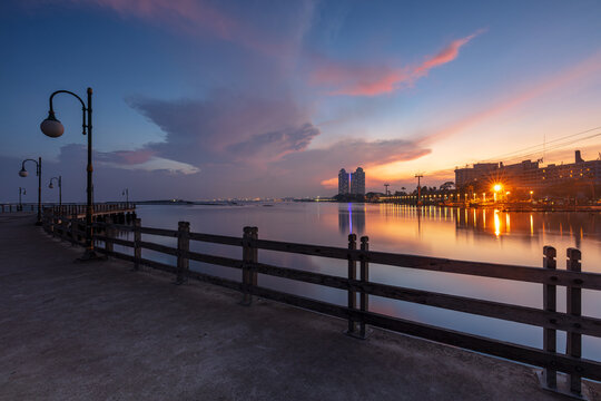 Tranquil Sunrise View with Leading Lines of a Wooden Pier and City Skyline at Ancol, Jakarta