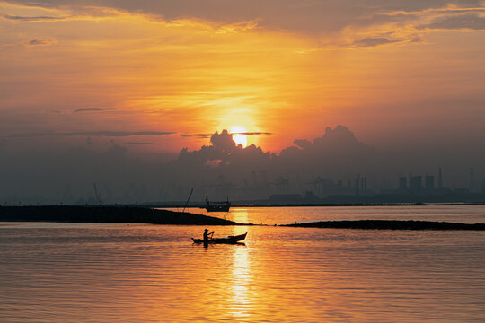 Atmospheric Sunrise Silhouette of a Fisherman in a Wooden Boat with Industrial Port Cranes in Jakarta Bay