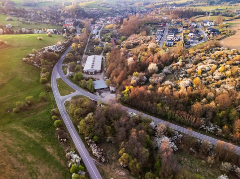 Aerial view of the village landscape featuring winding roads, residential houses, and blooming spring trees under golden hour light Cerin, Banska Bystrica Region, Slovakia.