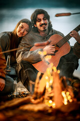 Fototapeta premium Friends enjoy music and warmth by the campfire near the lake on a cool evening