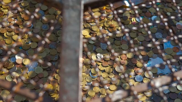 Coins and banknotes thrown in a metal grate. Coins and banknotes resting within metal grate, representing cultural tradition of making monetary offerings for bringing good luck and expressing hope