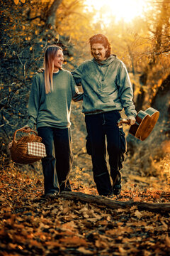 Couple walks through autumn woods while carrying a basket and guitar at golden hour