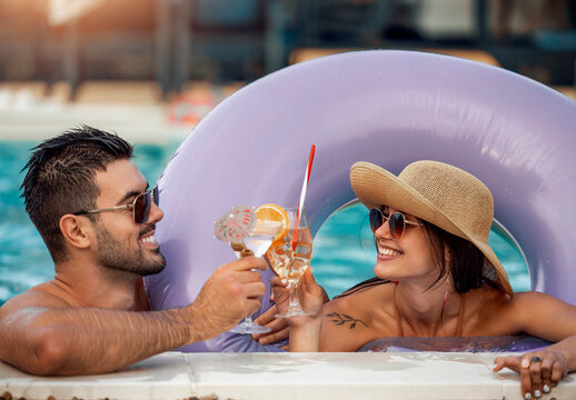 Couple enjoys drinks in a pool while relaxing in a float ring on a sunny day