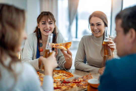 Friends enjoy pizza and drinks in a bright room during an evening gathering in a casual setting