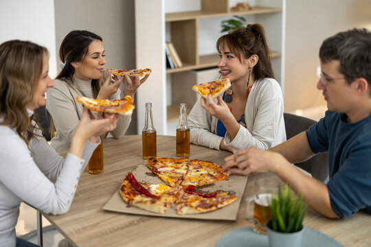 Group of friends enjoy pizza and drinks around a table in a cozy room during a casual evening gathering