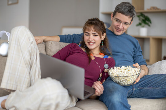 Couple enjoying a movie night at home with popcorn and laptop in a cozy living room setting during the evening