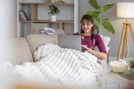 Young woman sits on couch with laptop and enjoys leisure time at home during an afternoon