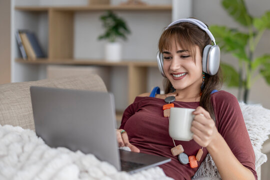 Woman smiling while enjoying coffee and working on laptop at home in cozy setting during afternoon
