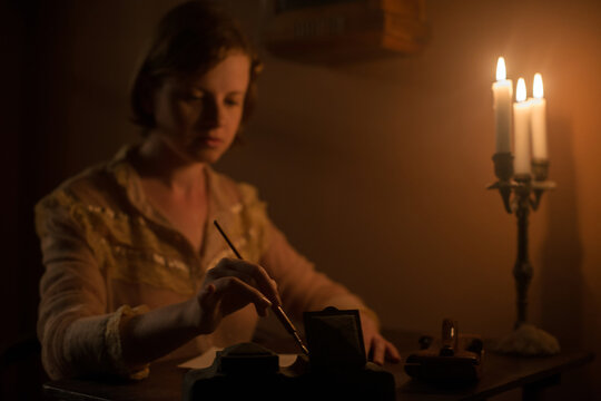 Young woman holding a dip pen writing a letter under candle light