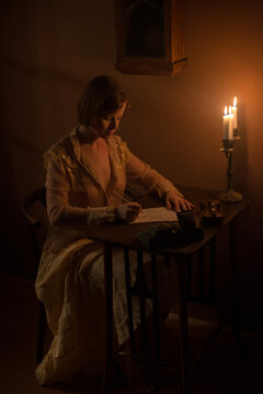 Young woman writing a letter under candle light