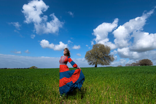 Young woman in a red dress in a green field with sky and clouds 