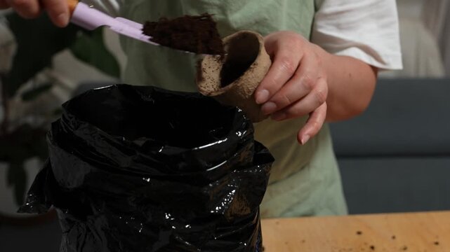 Gardener scoops rich earth into a biodegradable cup using a wooden-handled shovel 4k video. Filling Seedling Pots with Soil. Girl gardener fill a peat pot with dark soil.
