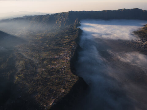 Aerial view of Bromo Tengger Semeru National Park with a sea of clouds filling the caldera and a village on the ridge Bromo, East Java, Indonesia.