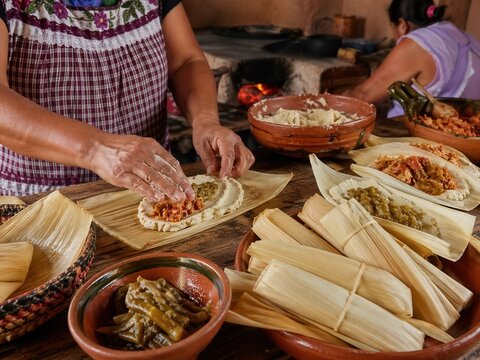 Traditionelle Tamales in rustikaler K&uuml;che herstellenFrau bereitet mehrere Tamales mit Maisteig und F&uuml;llung in einer authentischen traditionellen K&uuml;che zu.