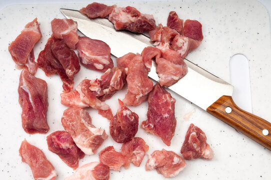Raw meat pieces and a kitchen knife on a modern white cutting board with dotted textures