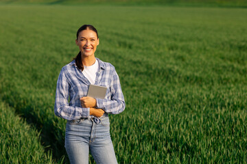 Naklejka premium Digital farm management. Female farm worker smiling and holding digital tablet standing in green field ready for harvest
