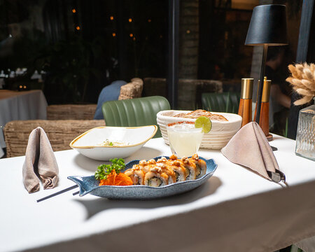 sushi de Salmon, en una mesa blanca dentro de un restaurante con servilletas de tela y cubiertos, sillas verdes y lampara para decorar 
