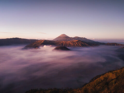 Aerial view of Mount Bromo and Mount Semeru rising above a thick sea of clouds during a purple sunrise in Bromo Tengger Semeru National Park Bromo, East Java, Indonesia.