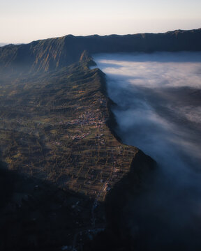 Aerial view of Bromo Tengger Semeru National Park with a mountain ridge village and thick fog filling the caldera during sunrise Bromo, East Java, Indonesia.