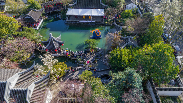 Aerial view of Lan Su Chinese Garden featuring a central pond with a dragon sculpture, traditional pavilions, and visitors surrounded by lush greenery in Portland, Oregon, United States.