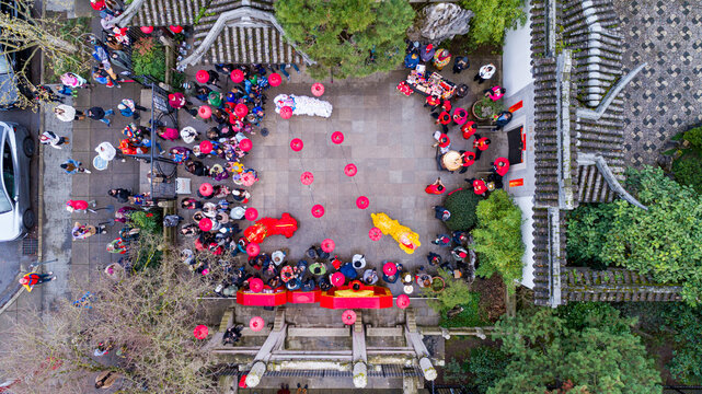 Aerial view of Lan Su Chinese Garden with people gathered in a courtyard for a lion dance performance and red lanterns in Portland, Oregon, United States.