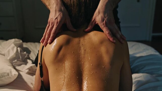 Man massaging bare sweaty back of woman on bed in bedroom interior, medium shot, close up, real time