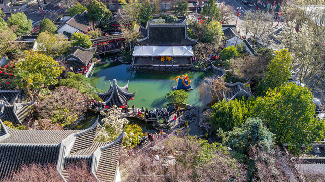 Aerial view of Lan Su Chinese Garden featuring traditional pavilions, a central pond with a dragon sculpture, and people on stone bridges in Portland, Oregon, United States.