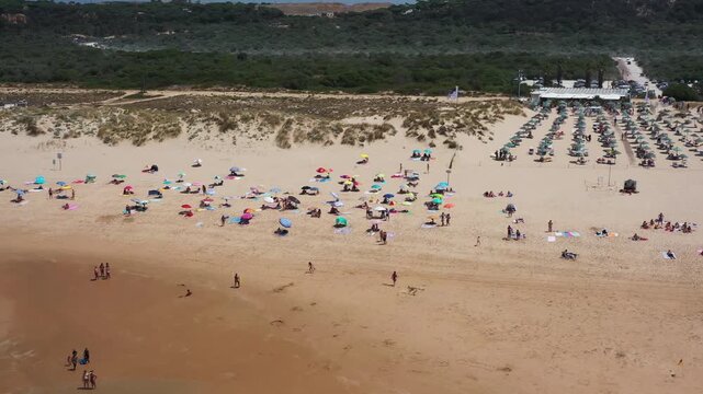 At the beach near Caparica in Portugal, people gather under colorful umbrellas. Visitors enjoy the sun and sand, creating a lively atmosphere by the shore.