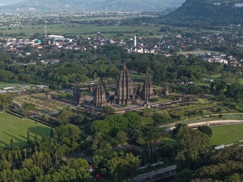 Aerial view of Prambanan Temple complex with its towering stone structures surrounded by lush green trees and the surrounding urban landscape Kecamatan Prambanan, Daerah Istimewa Yogya, Indonesia.