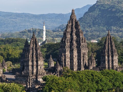 Aerial view of Prambanan Temple ancient stone spires rising above lush tropical trees with misty mountains in the background Kecamatan Prambanan, Daerah Istimewa Yogya, Indonesia.