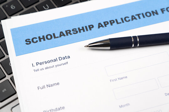 A close-up shot of a blue and white scholarship application form placed on a laptop keyboard, featuring a professional blue ballpoint