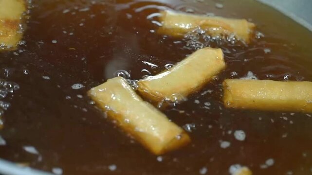 Crispy spring rolls frying in hot oil, golden Asian street food snack close-up with bubbling texture and savory market food vibe.