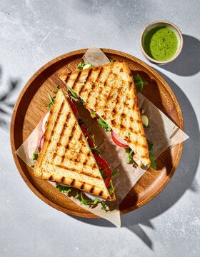 Delicious grilled sandwiches on wooden plate with green sauce