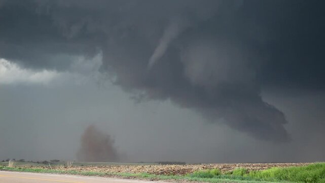 A tornado churns dirt in the prairie in Nebraska. Grass can be seen waving in the wind.