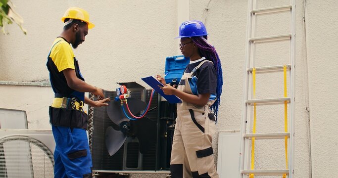 Diverse team of capable electricians brainstorming possible ways to repair damaged outdoor hvac system. Seasoned wiremen colleagues commissioned to fix broken air conditioner