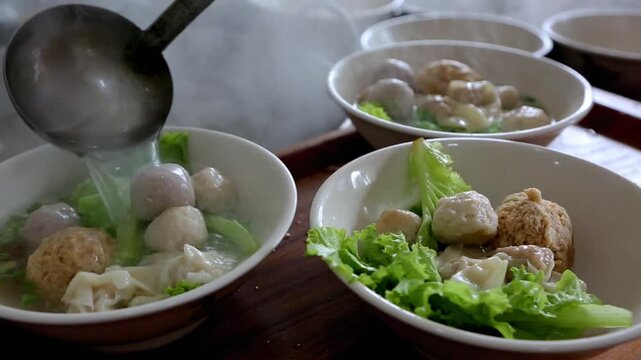 Steaming Asian meatballs and dumplings with green vegetables in a white bowl on a wooden table, close-up of traditional comfort food.